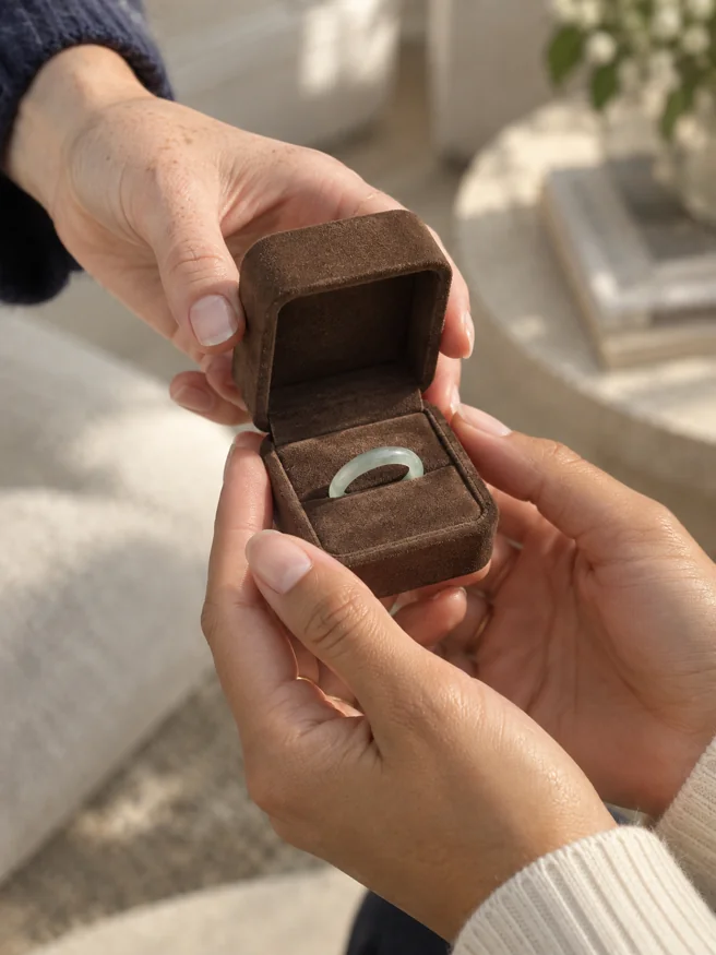 Two hands exchanging a jade ring in a gift box